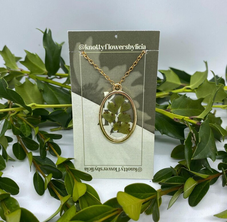handmade resin necklace with a fern leaf as the centerpiece of the gold oval shaped pendant